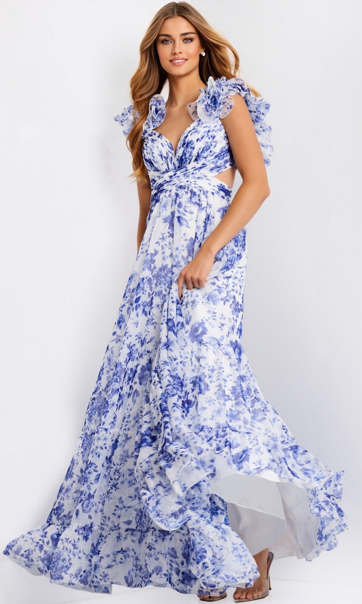 A woman in the Jovani 49143 Ruffled Long Print Prom Dress, featuring blue floral patterns, ruffled sleeves, and a flowing skirt, stands against a plain light background.